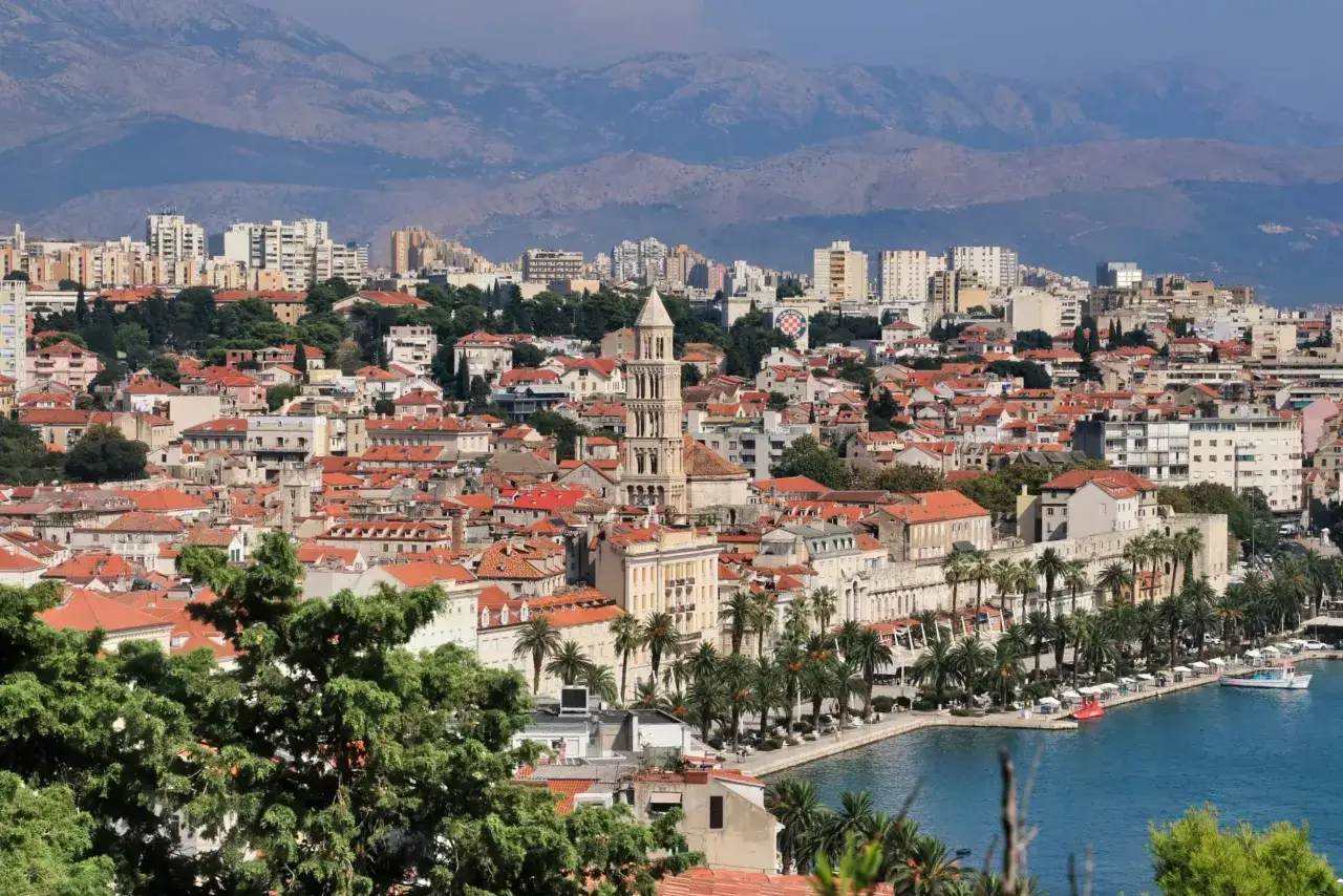 Widok na miasto Split z palmami, morzem i górami w tle. Widać zabytkową architekturę i nowoczesne budynki, tworzące unikalne atrakcje.