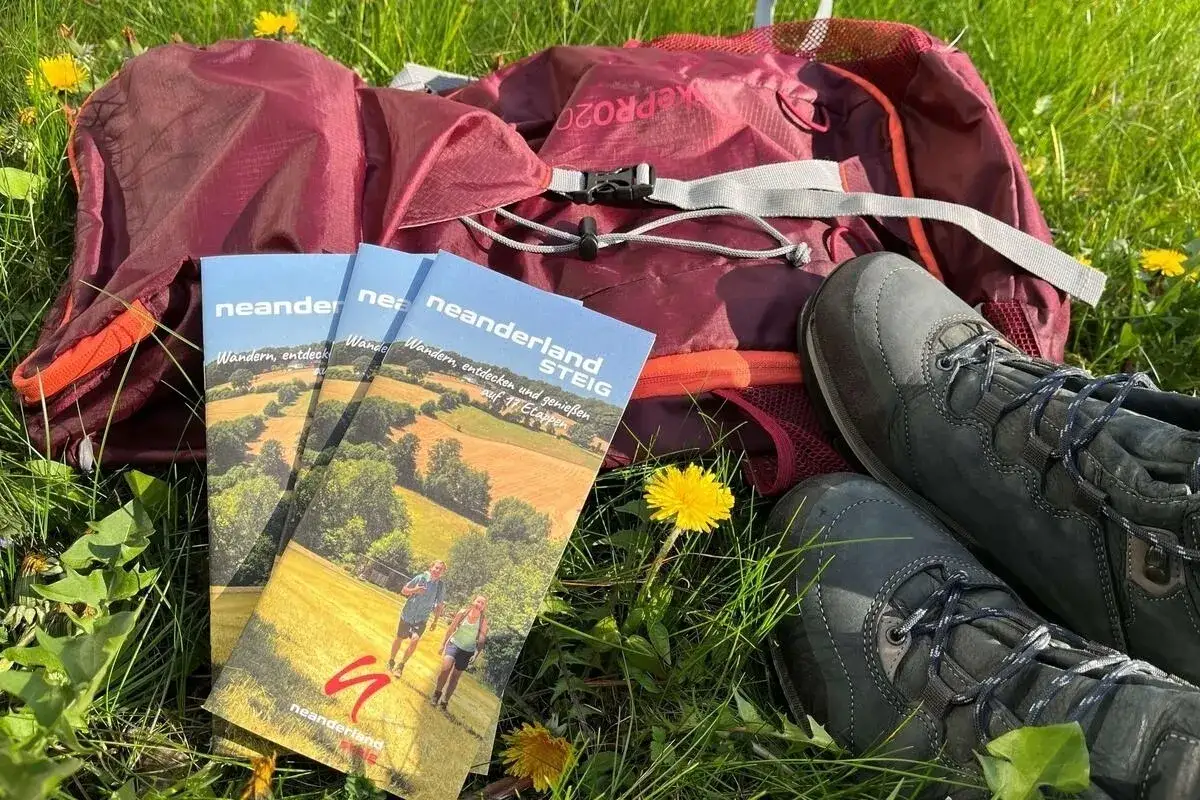 Wanderstiefel, Rucksack und Brosch&uuml;ren f&uuml;r die neanderlandsteig rundwege liegen im Gras. Bereit f&uuml;r das n&auml;chste Abenteuer!