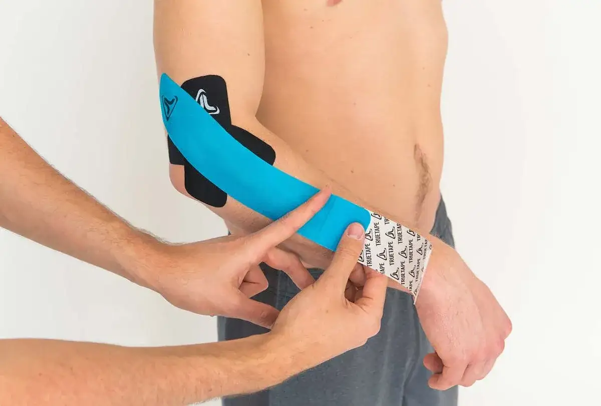 Tennisarm tapen sinnvoll: Ein Arm wird mit blauem und schwarzem Kinesiotape versorgt, um Schmerzen zu lindern.