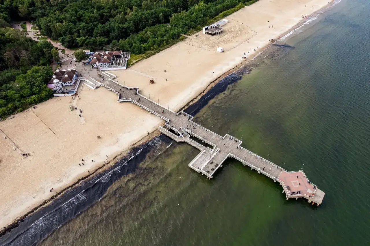 Molo w Brzeźnie, plaża i zielone morze. Spacerowicze podziwiają brzeźno atrakcje.