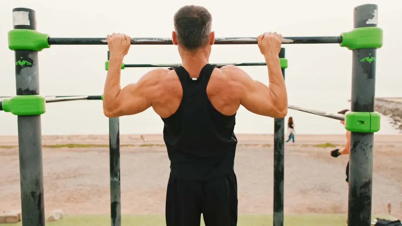Un homme muscl&eacute; s'entra&icirc;ne sur une barre de traction, suivant son programme traction.