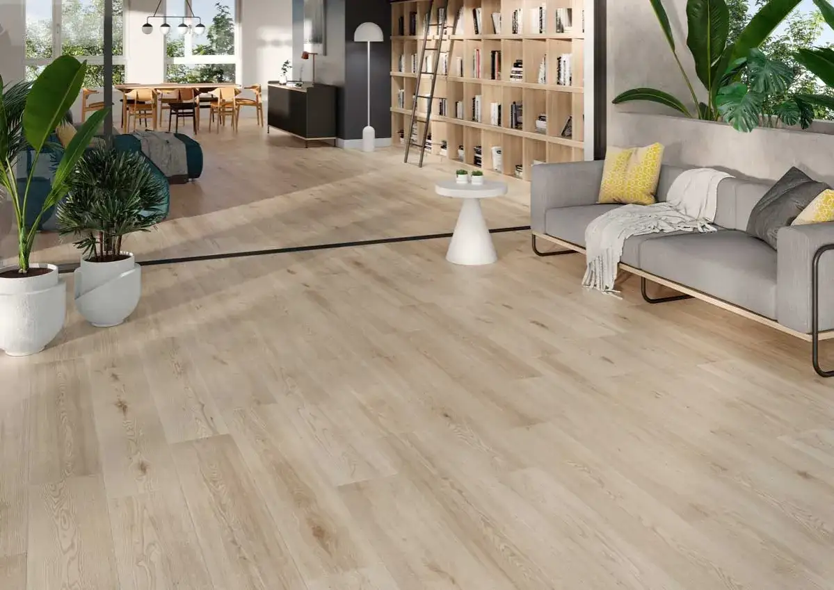 Amplio sal&oacute;n con suelo de porcelanico rectificado de madera clara, sof&aacute; gris, estanter&iacute;as y plantas.