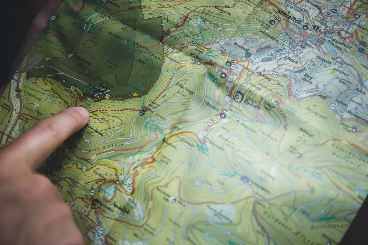 Finger zeigt auf Karte mit Wanderwegen und H&uuml;tten. Planung von **Trekking Camps Deutschland**.