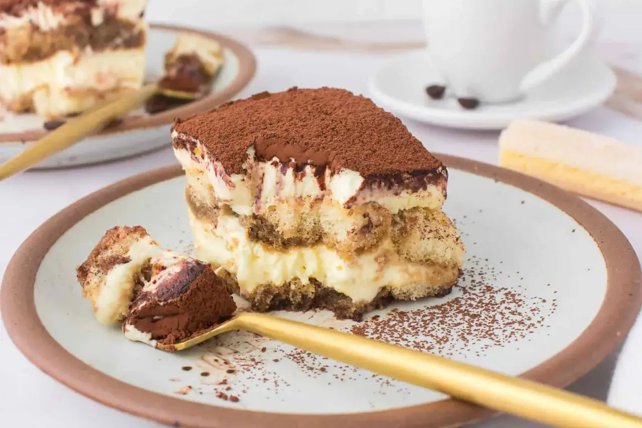 Ein St&uuml;ck cremiges Tiramisu, das nach dem original italienischen Rezept zubereitet wurde, mit L&ouml;ffel und Kakaopulver.