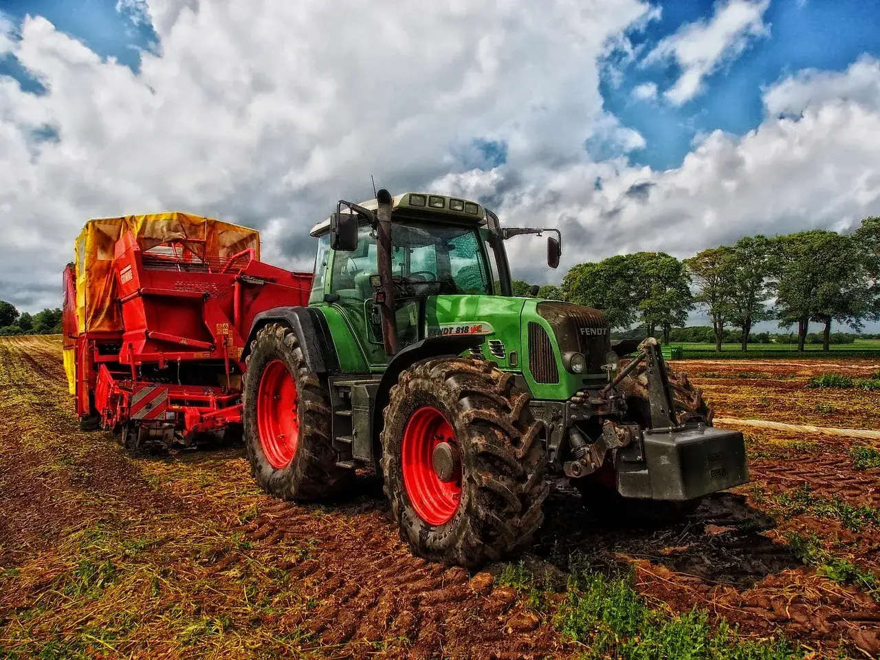Zielony traktor z przyczepą na polu. Traktorzysta przygotowuje się do pracy.