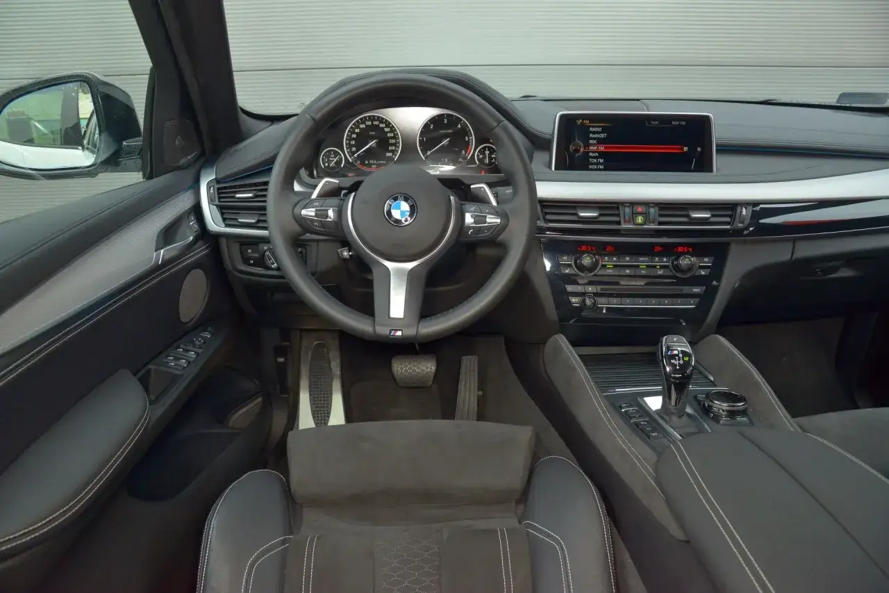 Wnętrze BMW F16 z czarną tapicerką, kierownicą M i ekranem multimedialnym.