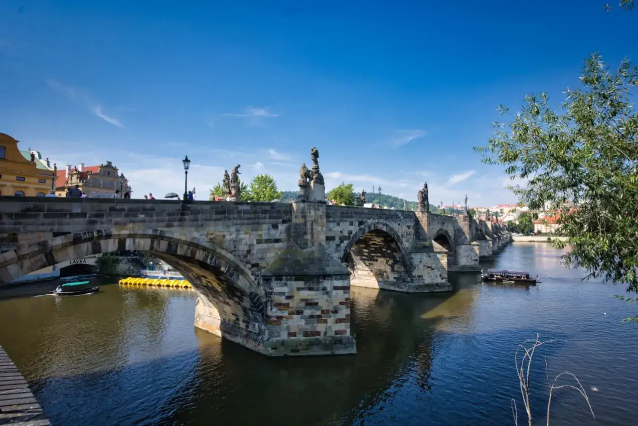 Karlsbr&uuml;cke in Prag, ein Wahrzeichen f&uuml;r Prag Sightseeing, mit Statuen, Booten auf der Moldau und blauer Himmel.