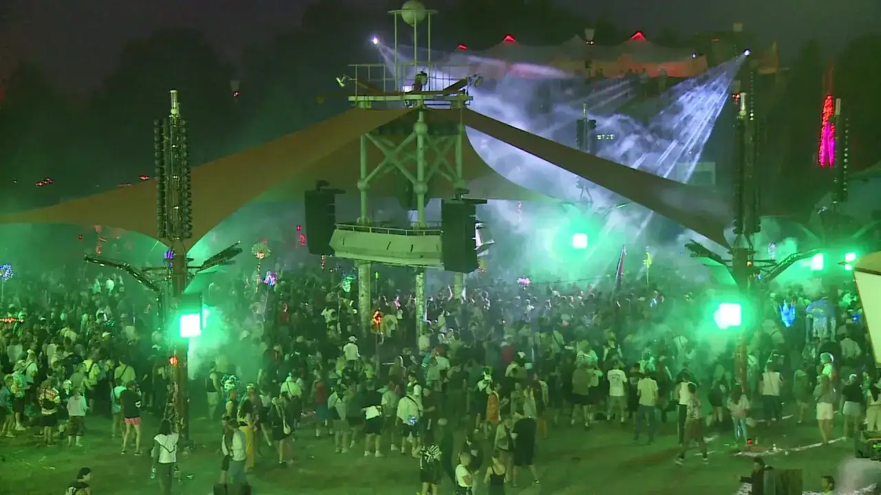 Fusion Festival Logo: Eine Menschenmenge tanzt unter gr&uuml;nen Lichtern und Nebel, w&auml;hrend eine B&uuml;hne mit Lautsprechern und Lichtern im Hintergrund beleuchtet wird.