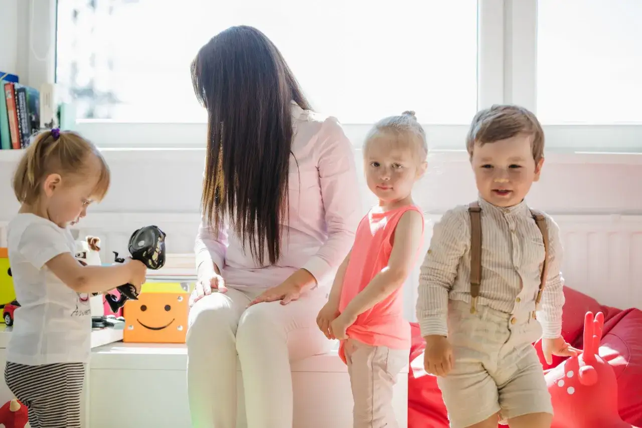 Niania z trójką dzieci w pokoju zabaw. Dzieci bawią się zabawkami, a niania siedzi obok. Zastanawiasz się, ile biorą nianie za godzinę?