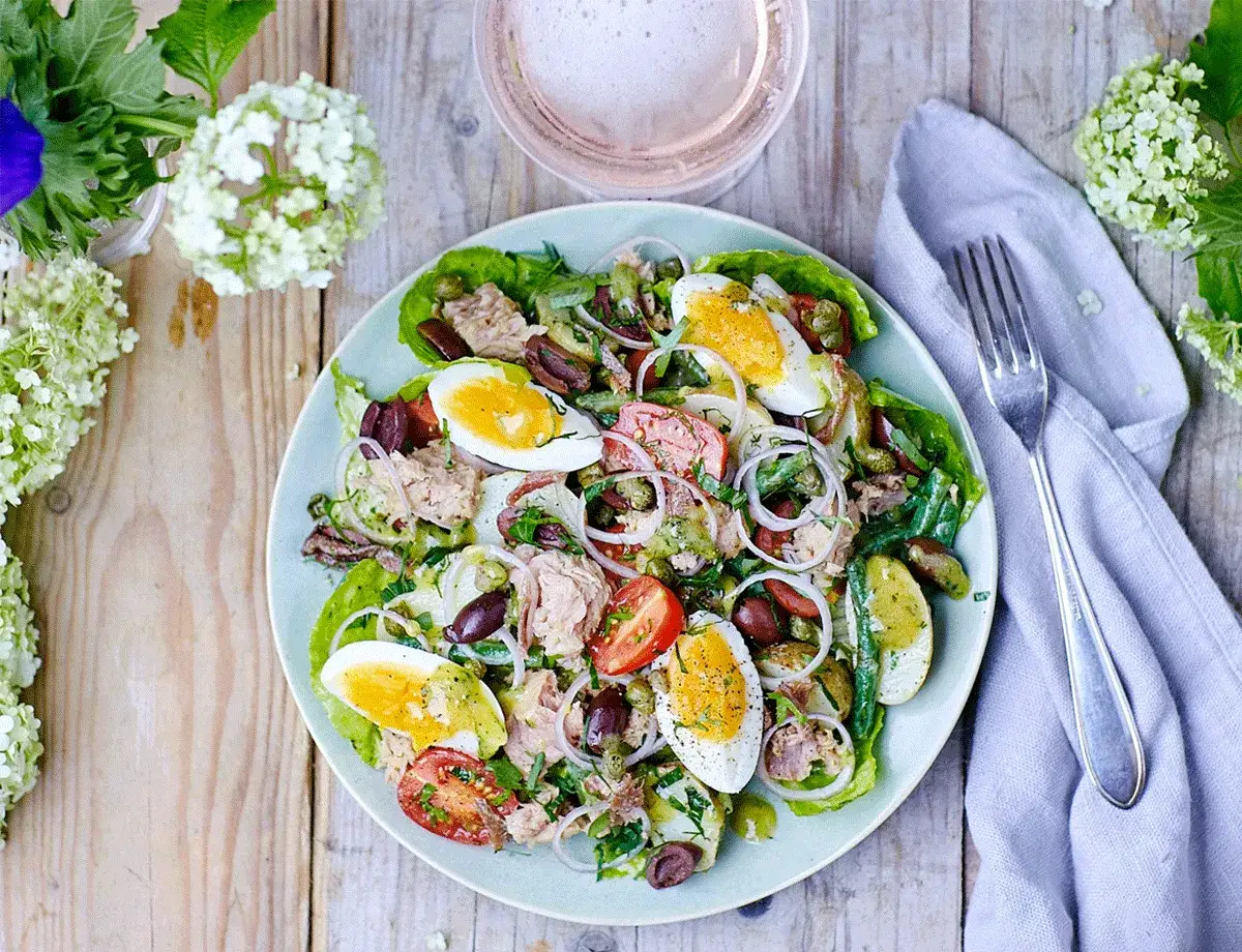 En h&auml;rlig sallad nicoise med tonfisk, &auml;gg, gr&ouml;na b&ouml;nor, oliver och tomater, serverad p&aring; en ljusbl&aring; tallrik.