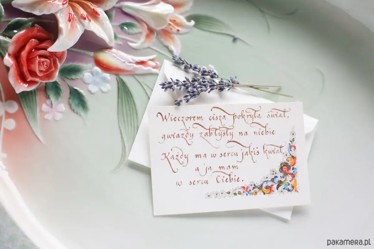 Kr&oacute;tki wiersz o kwiatach na kartce z lawendą, obok ceramicznych r&oacute;ż i lilii.