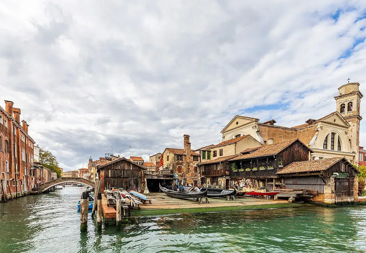 Lo squero di San Trovaso, con le sue botteghe di maestri d'ascia, gondole in lavorazione e il canale che riflette il cielo nuvoloso.
