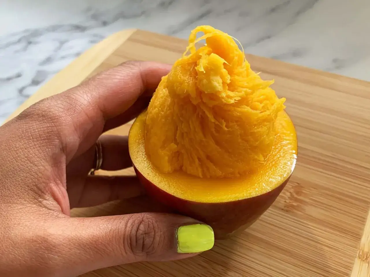 Ręka trzyma przekrojone mango, ukazując jego soczysty, włóknisty miąższ. To owoc pełen witamin, a jego mango właściwości doceniane są od wieków.
