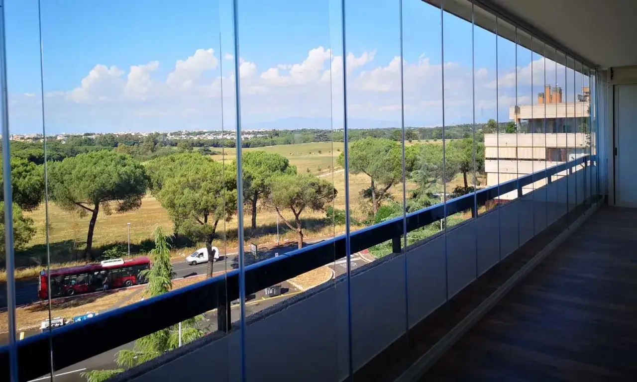 Veranda chiusa con vetrate scorrevoli, vista su parco alberato e citt&agrave;. Ideale per chi cerca una chiusura veranda normativa e funzionale.