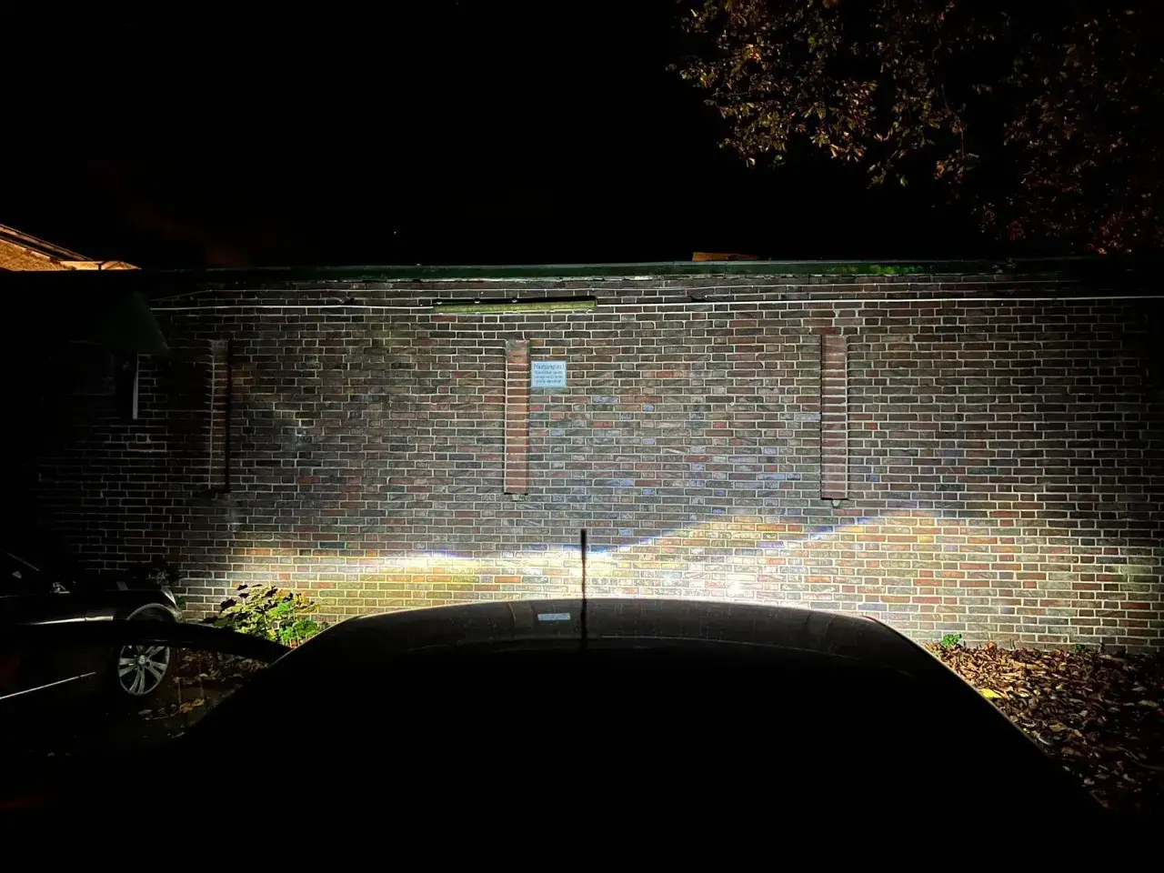 Bilens h7 led-str&aring;lkastare lyser upp en tegelv&auml;gg i m&ouml;rkret.