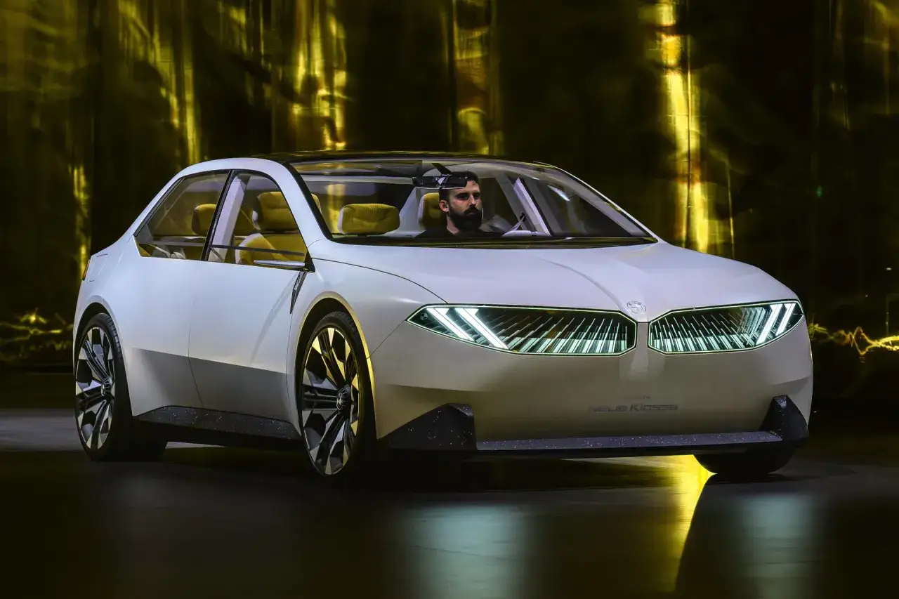 Wei&szlig;er BMW i3 Neue Klasse mit gelben Sitzen und einem Mann am Steuer, beleuchtet von gelbem Licht.