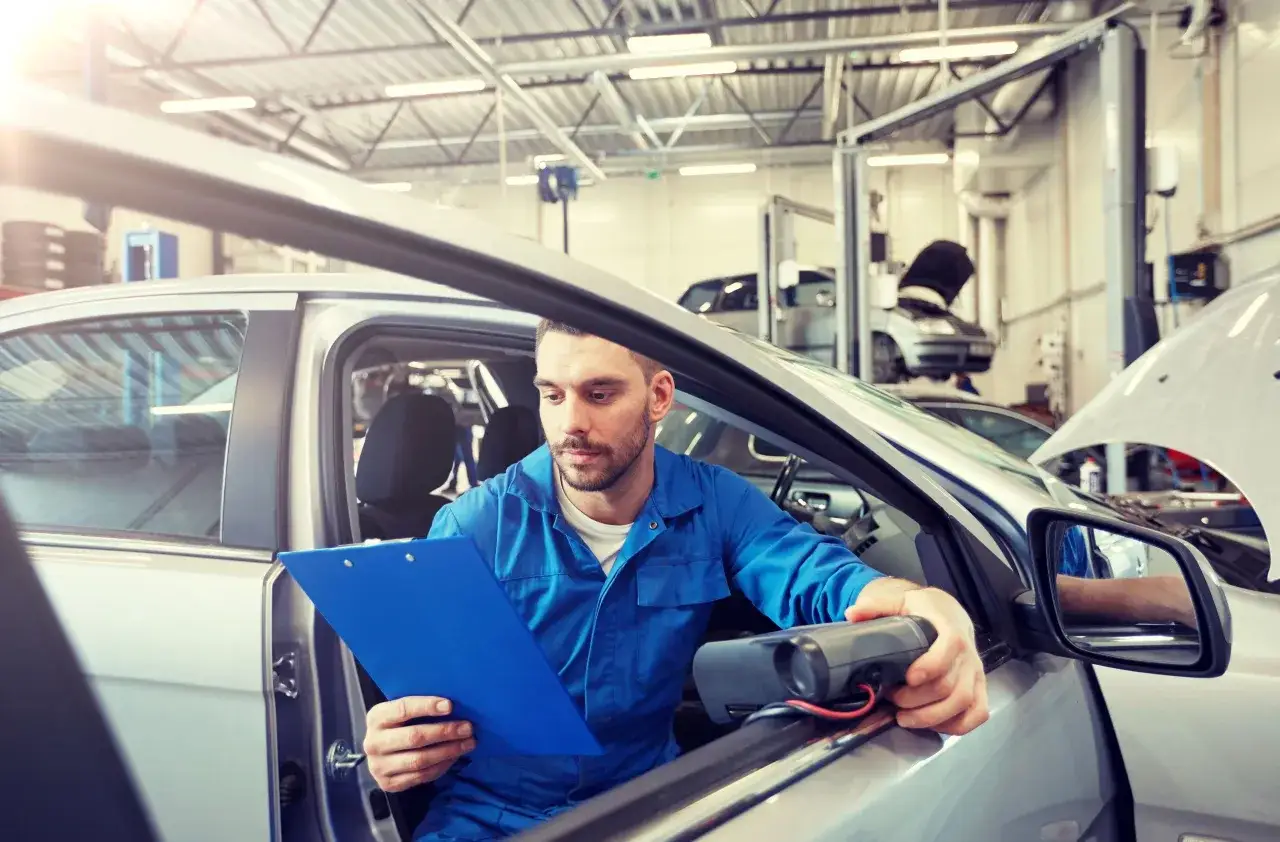 Meccanico con cartella blu e strumento di diagnosi, controlla l'allestimento auto libretto.