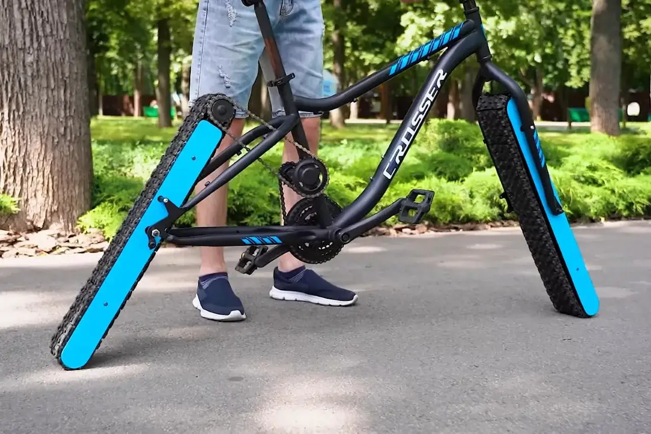 A person stands beside some weird bikes with tank-like treads instead of wheels.