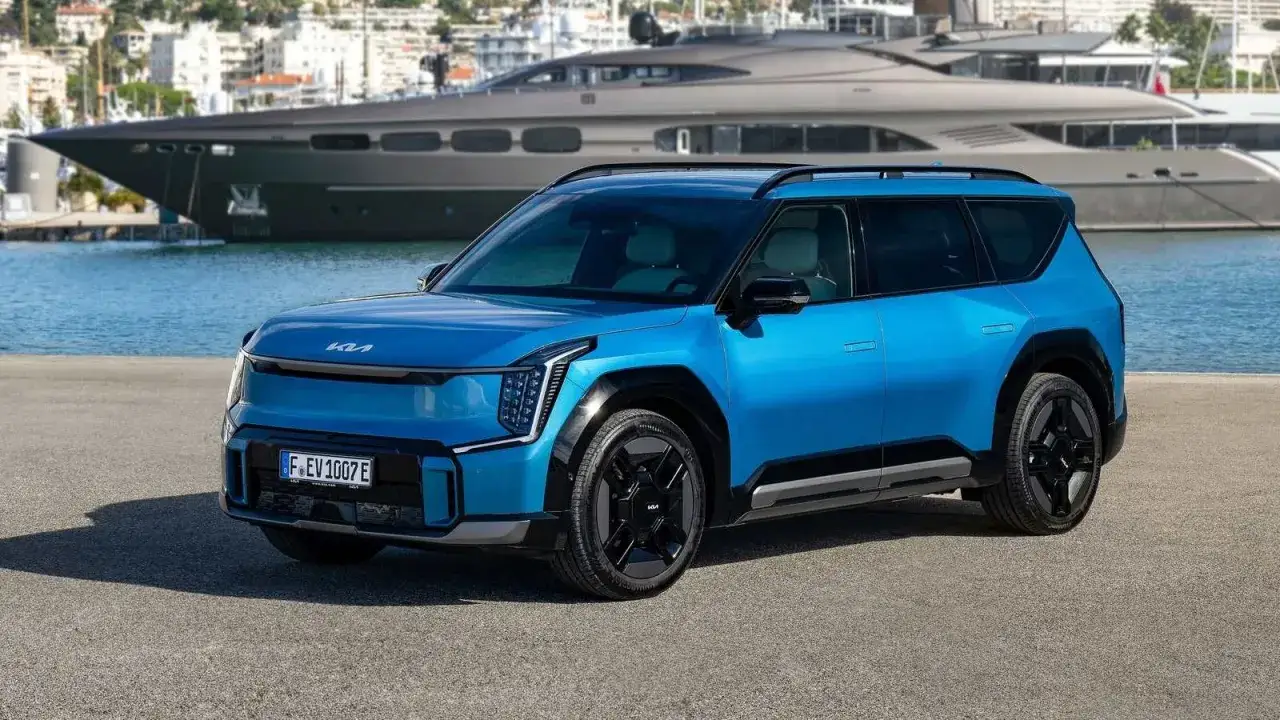 Un SUV azul eléctrico, uno de los coches cómodos ideales para explorar la costa, aparcado frente a un yate de lujo y un puerto.