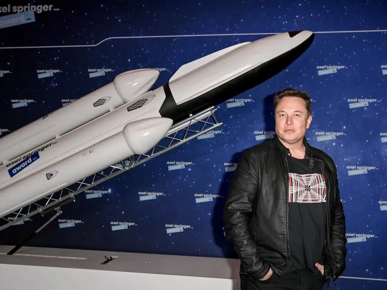 Elon Musk, wizjoner i tw&oacute;rca SpaceX, stoi obok modelu rakiety.