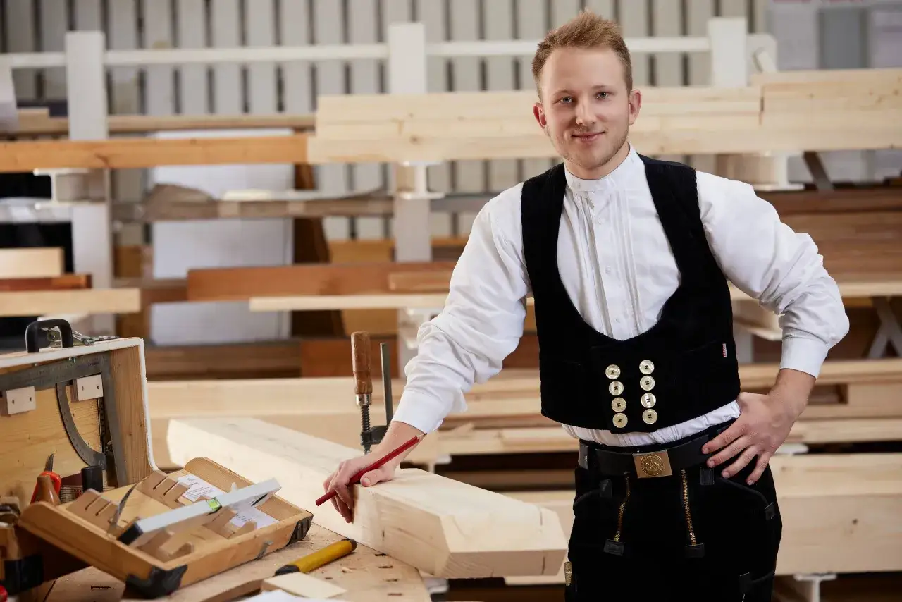 Ein junger Zimmermann in traditioneller Kleidung, der an einem Holzst&uuml;ck arbeitet. Die zimmerer ausbildung gehalt netto ist ein wichtiges Thema f&uuml;r angehende Handwerker.