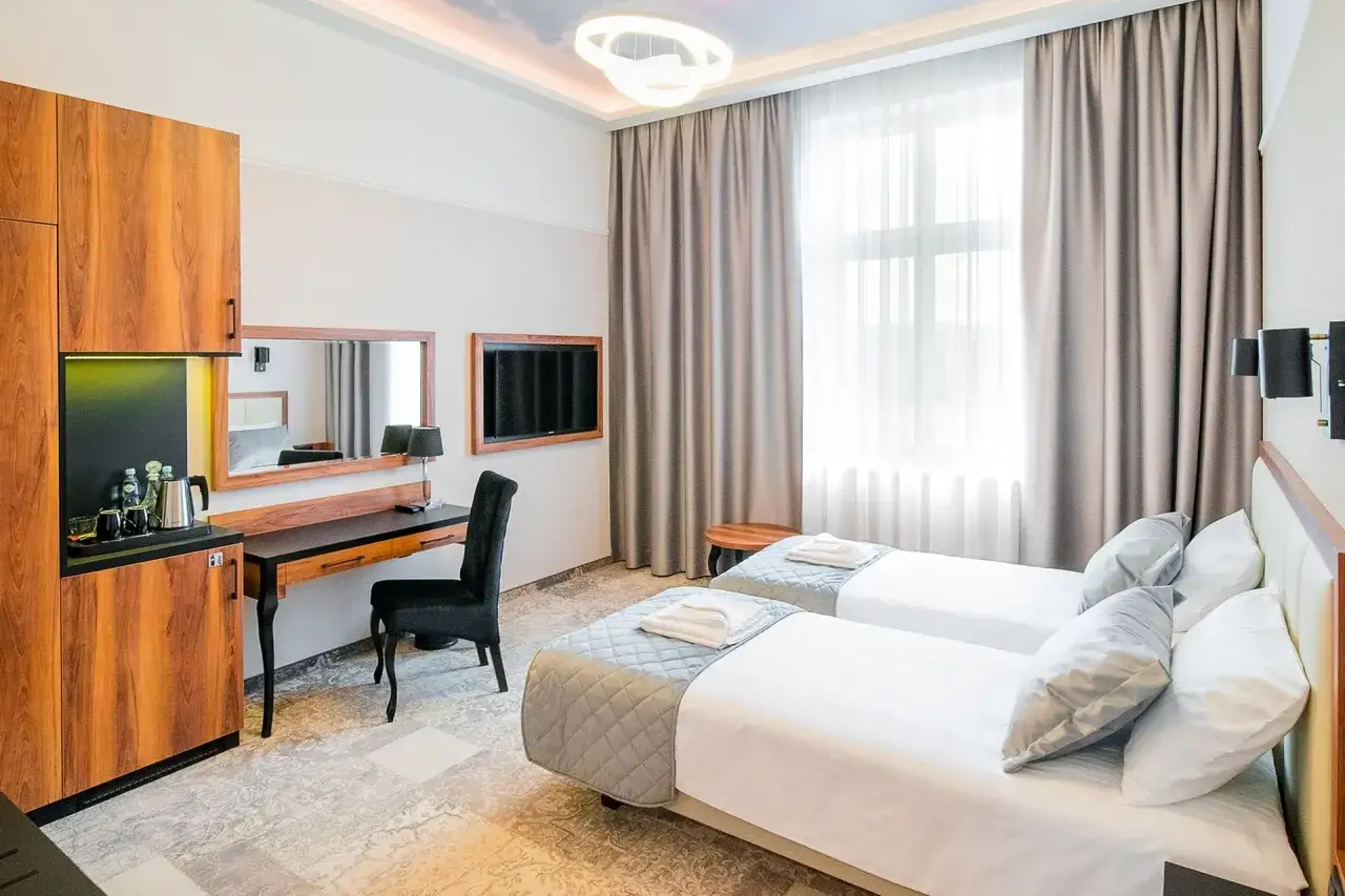 Pokój hotelowy z dwoma łóżkami, biurkiem i aneksem kuchennym. Zastanawiasz się, ile kosztuje doba w hotelu?