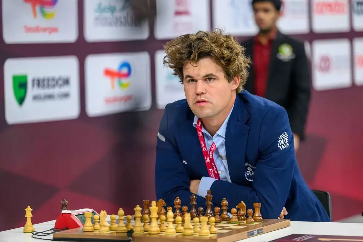 Magnus Carlsen, aktualny mistrz świata w szachach, siedzi przy szachownicy, gotowy do gry.