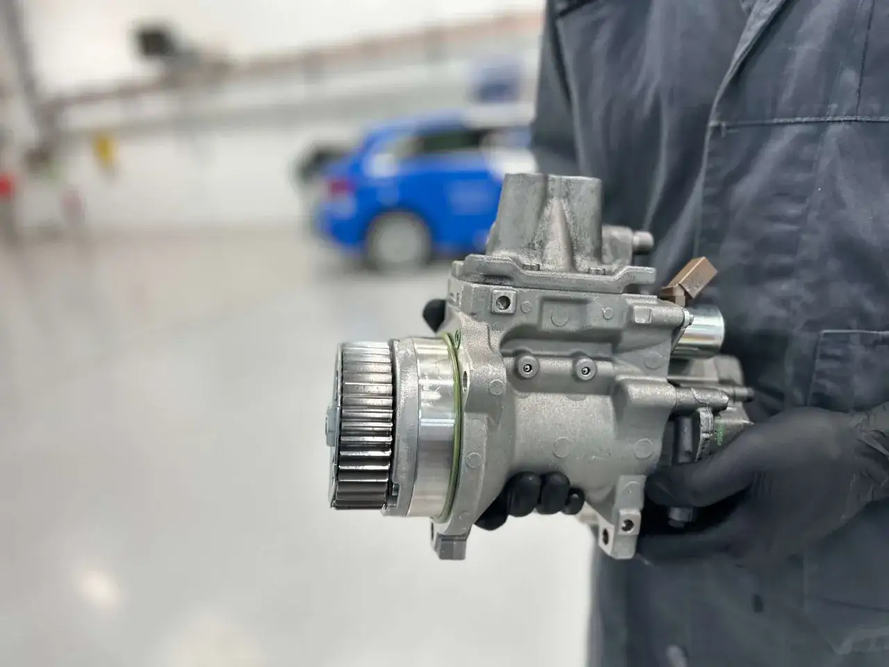Mechanik w czarnej rękawiczce trzyma pompę paliwa. Czy to Delphi? To firma znana z części samochodowych.