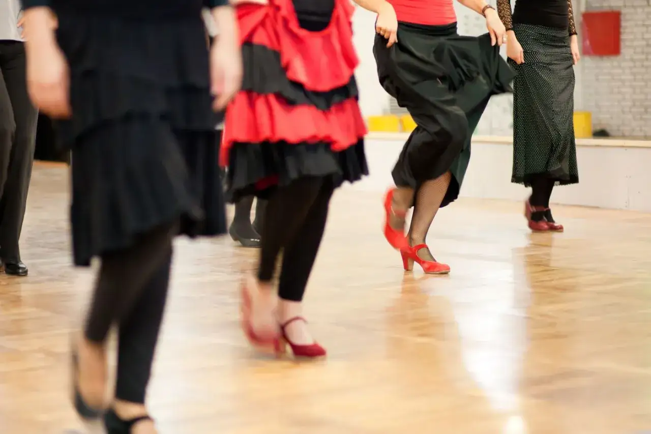 Clase de baile flamenco para principiantes. Mujeres con faldas y tacones rojos mueven sus pies en un salón de baile.