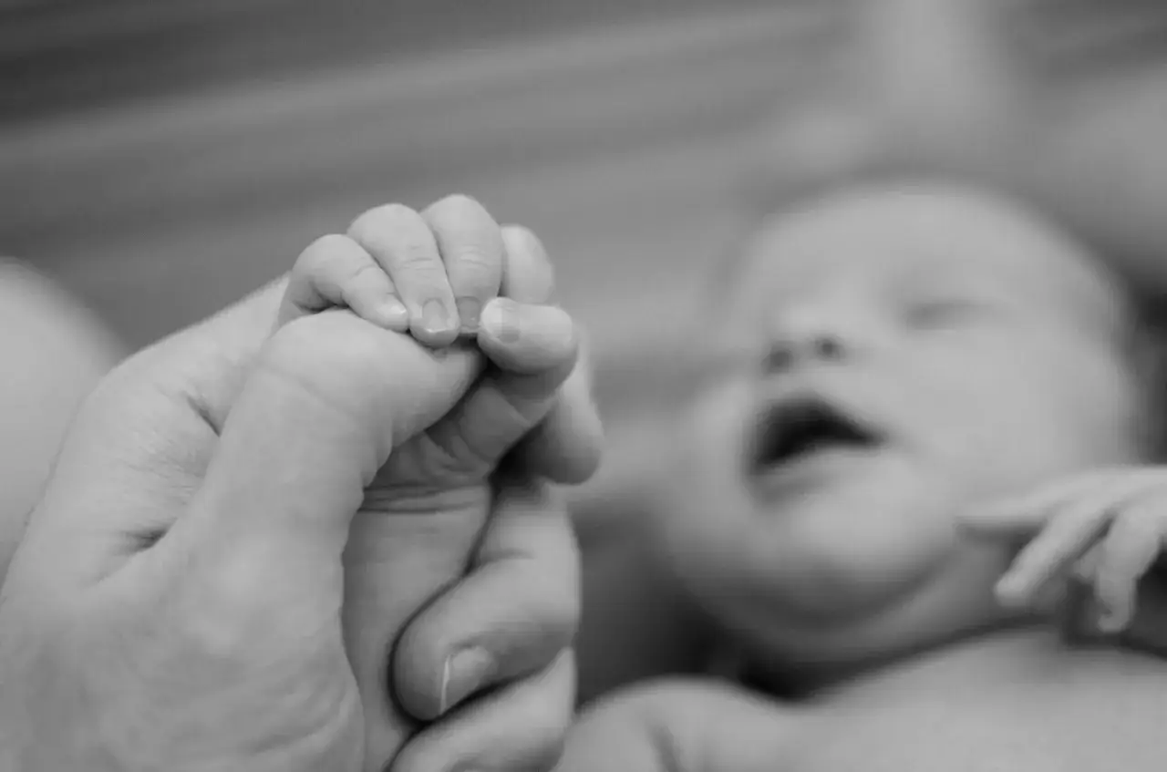 Dłoń dorosłego obejmuje maleńką dłoń dziecka. Ten moment symbolizuje, kiedy wcześniak przestaje być wcześniakiem, stając się silniejszy.