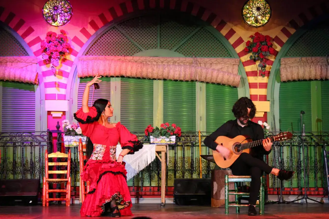 Bailaora de flamenco andaluz con vestido rojo y casta&ntilde;uelas, acompa&ntilde;ada por un guitarrista.