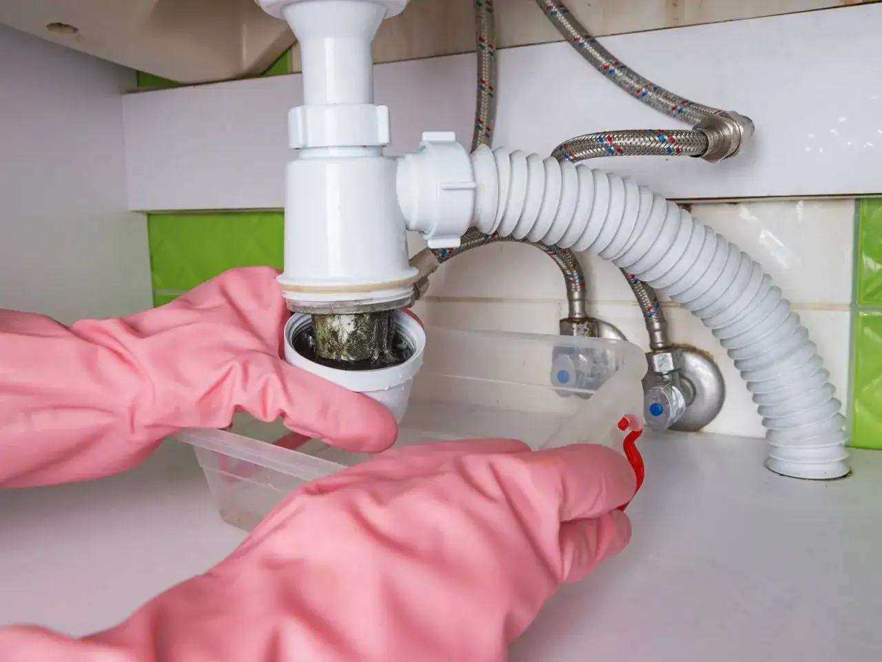 Nettoyage du siphon d'&eacute;vier de cuisine. Mains gant&eacute;es retirant un filtre obstru&eacute; par des d&eacute;bris.
