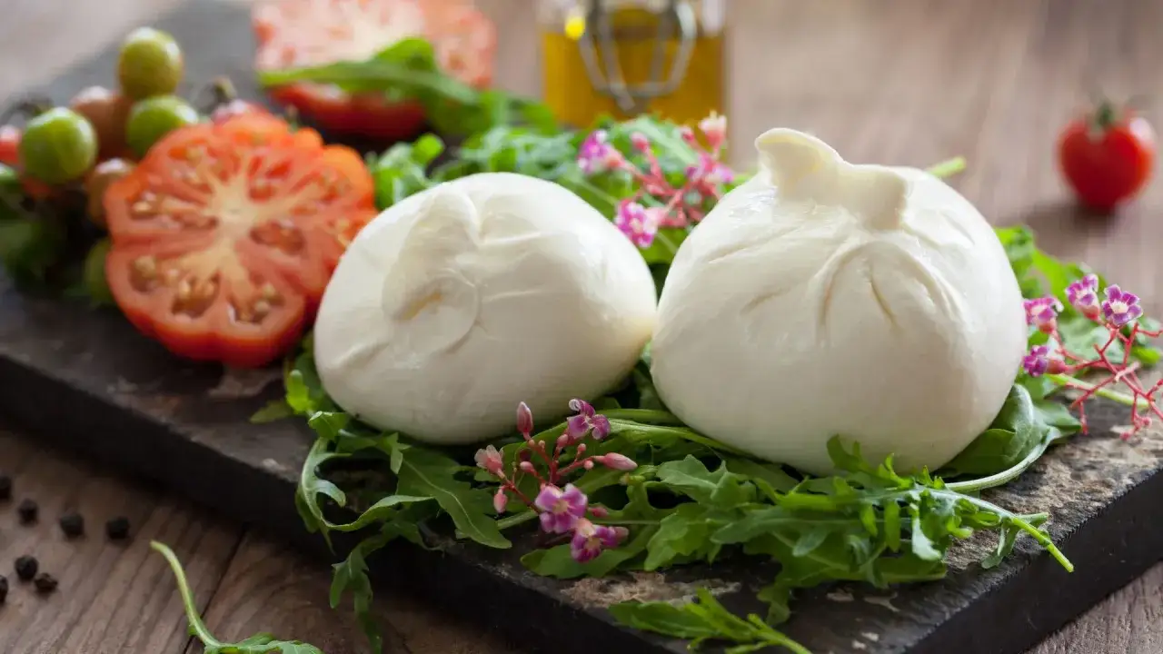 Dwie kulki burraty, świeże pomidory i rukola na desce. Czy wiesz, burrata co to?