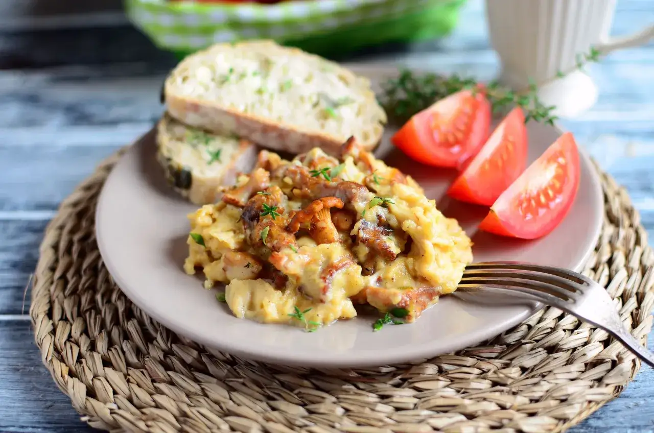 Pyszna jajecznica z kurkami, podana z chlebem i pomidorami. Idealne śniadanie dla miłośników leśnych smaków.