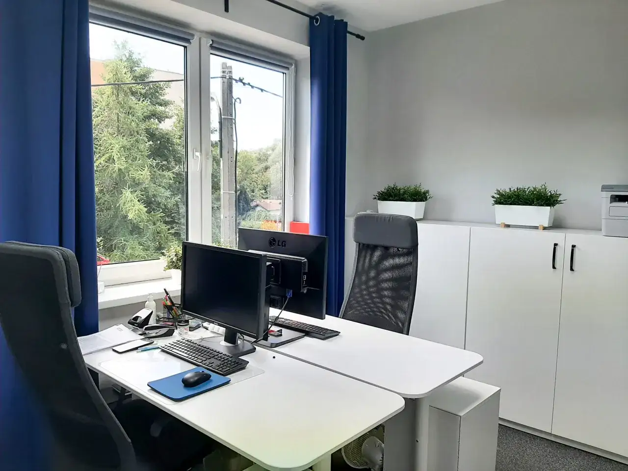 Nowoczesne biuro z dwoma stanowiskami pracy, monitorami i roślinami.