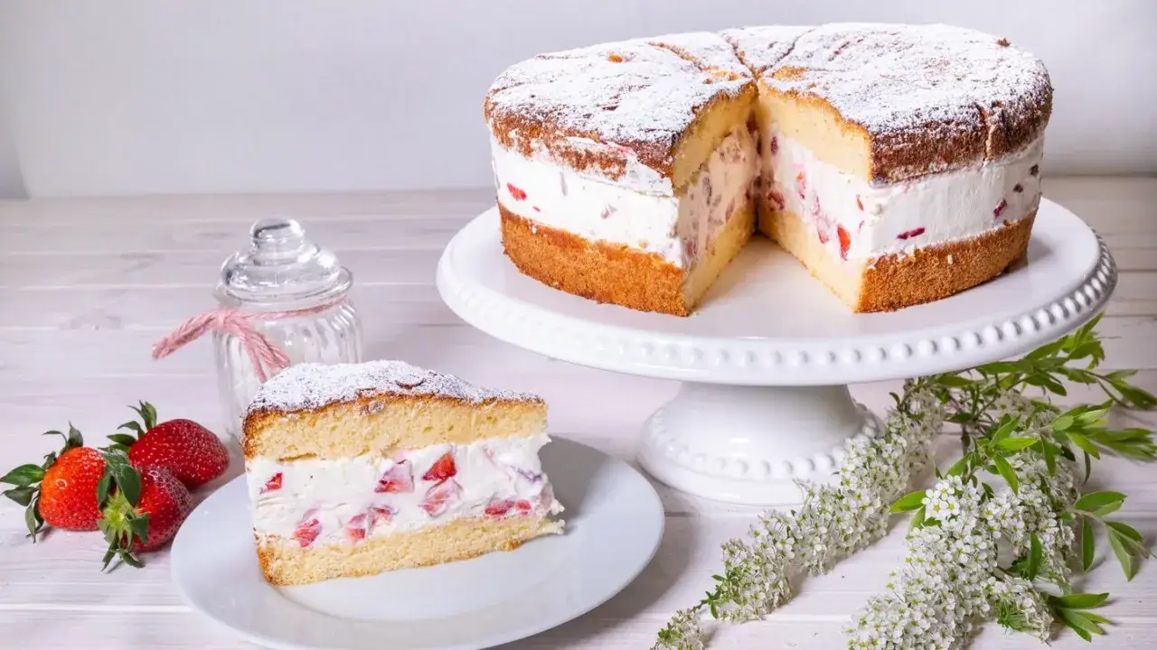 Eine k&ouml;stliche Erdbeer Sahne Torte, mit frischen Erdbeeren und Puderzucker best&auml;ubt, wartet darauf, genossen zu werden. Ein St&uuml;ck ist bereits auf einem Teller angerichtet.