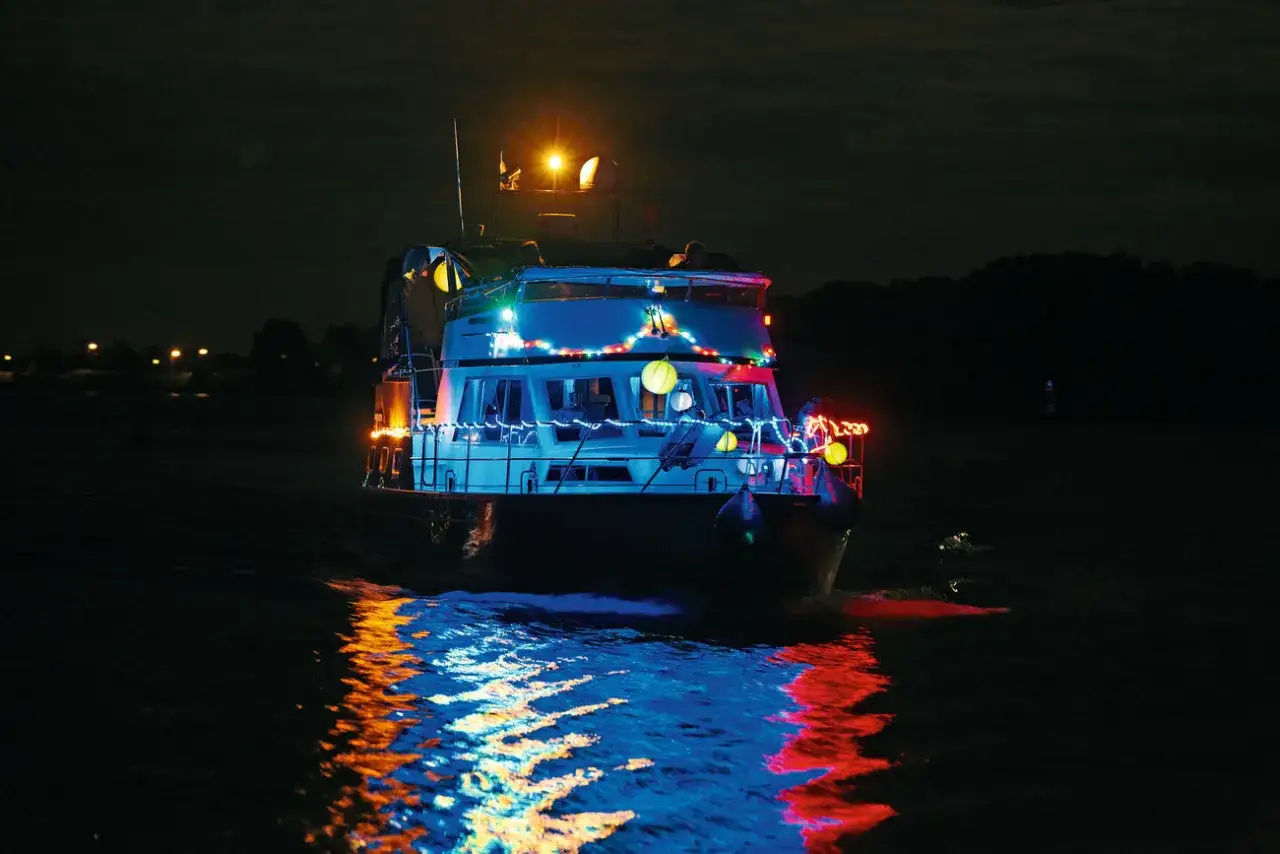 Festlich beleuchtetes Boot unter 7 Meter Länge gleitet nachts über das Wasser, bunte Lichter spiegeln sich im dunklen Wasser.