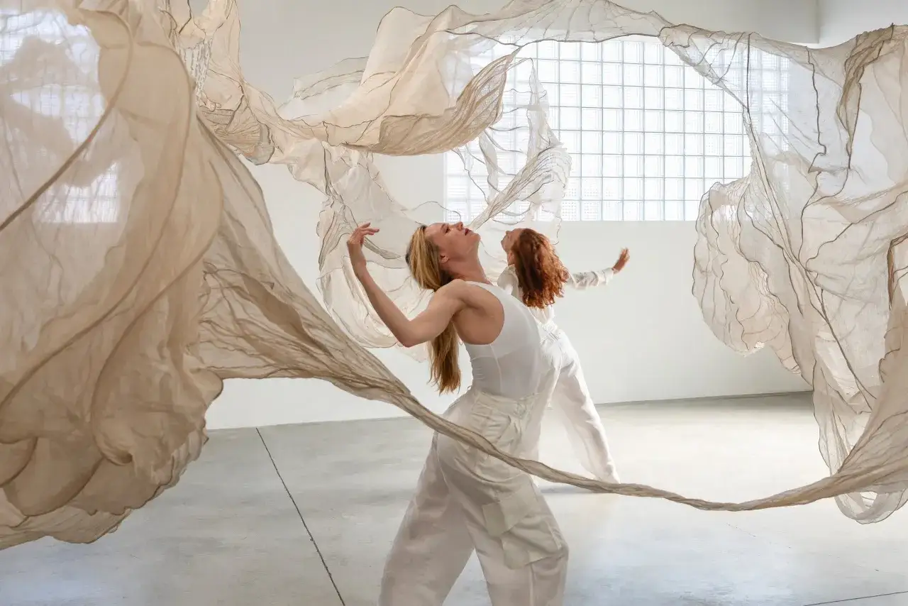 Dos bailarinas interactúan con telas etéreas, explorando la fluidez y el movimiento. Una escena que evoca la pregunta: ¿qué es el arte contemporáneo?