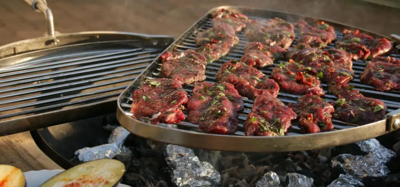 Saftiges **Grillfleisch** mit Kräutern liegt auf dem Rost. Dampf steigt auf, während die Kohlen darunter glühen. Ein Fest für die Sinne!
