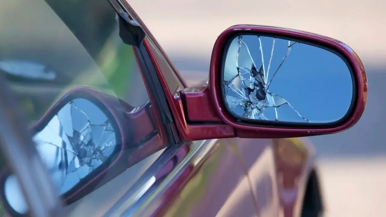 Specchietto rotto dell'auto, con il vetro frantumato che riflette il cielo.