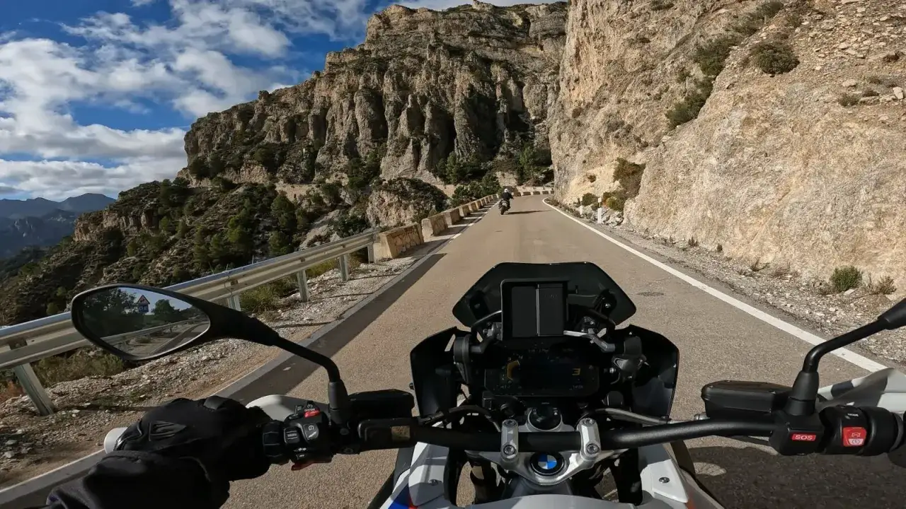 Jazda motocyklem po krętej drodze w górach Hiszpanii, z widokiem na skaliste zbocza i błękitne niebo.