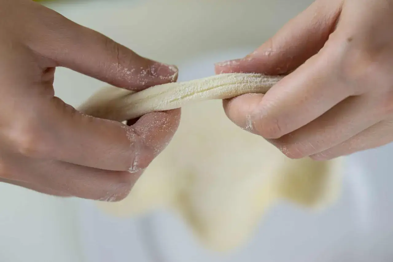 Dłonie formują ciasto, przygotowując szybki przepis na ciasto do pizzy. Mąka lekko oprósza palce.