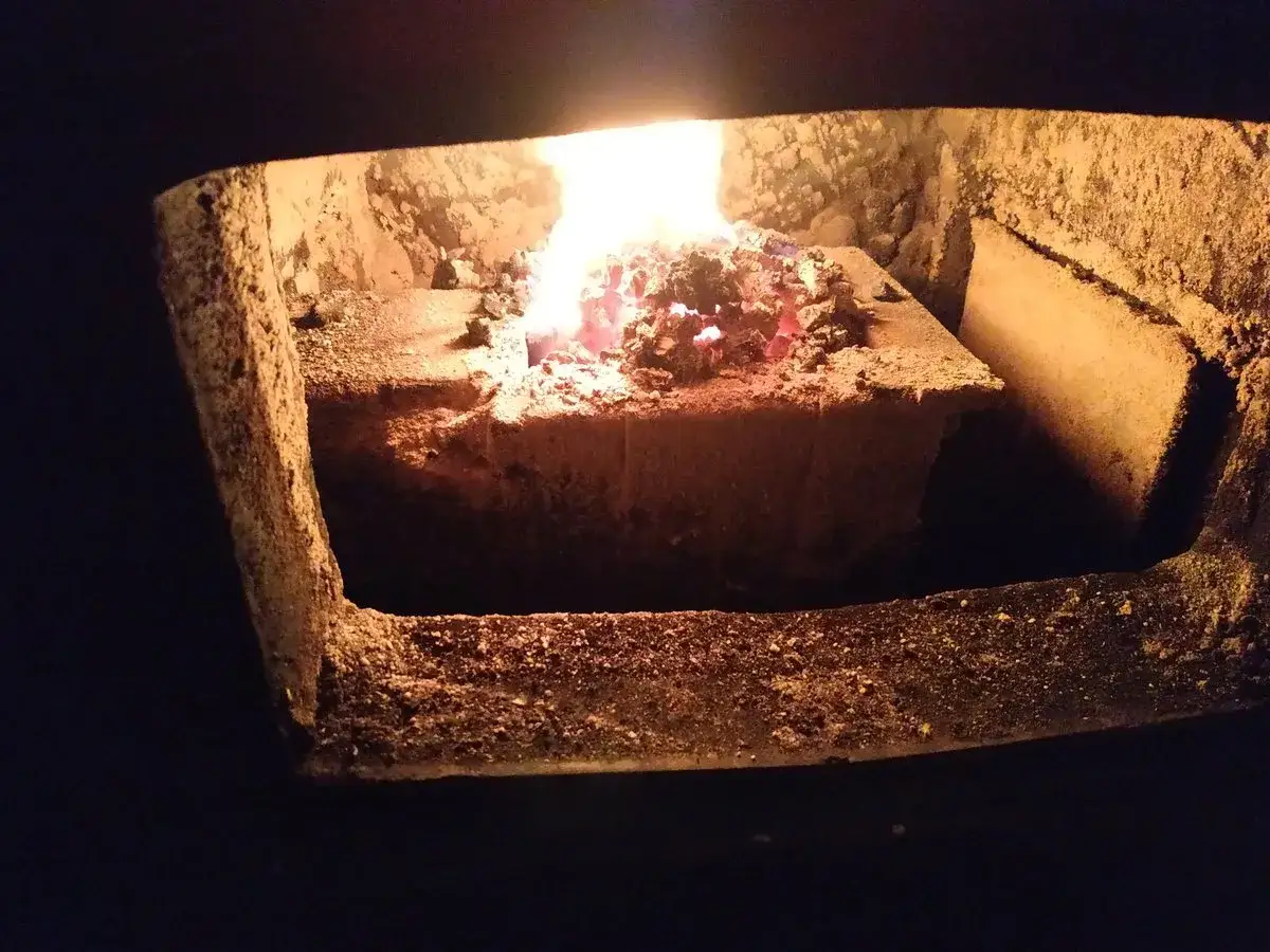 Żarzący się, niedopalony ekogroszek w popielniku. Płomienie tańczą nad resztkami paliwa, tworząc ciepły blask.