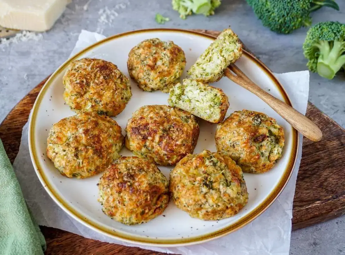 Goldbraune, knusprige **Broccoli Nuggets** auf einem Teller, daneben frischer Brokkoli und ein St&uuml;ck K&auml;se.