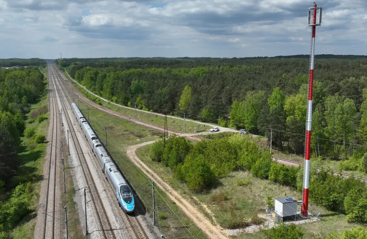 Szybki pociąg mknie po torach, a obok niego stoi wieża zapewniająca łączność radiową.