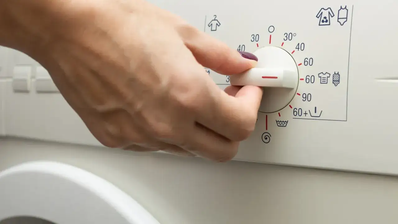 Dłoń ustawia pokrętło pralki na 60 stopni. Zastanawiasz się, ile trwa pranie w 60 stopniach?