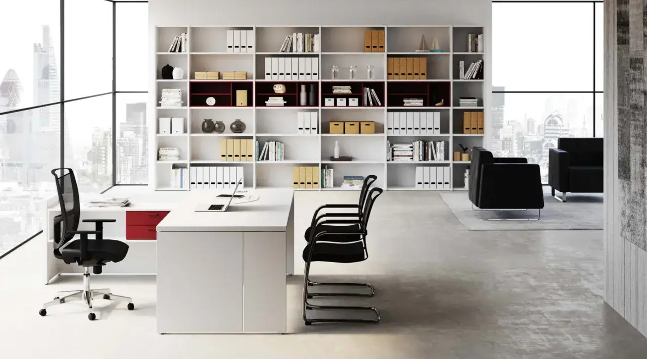 Arredamento studio psicologo: scrivania bianca, scaffalature piene di libri e oggetti, sedie nere, poltrone in pelle e vista sulla città.