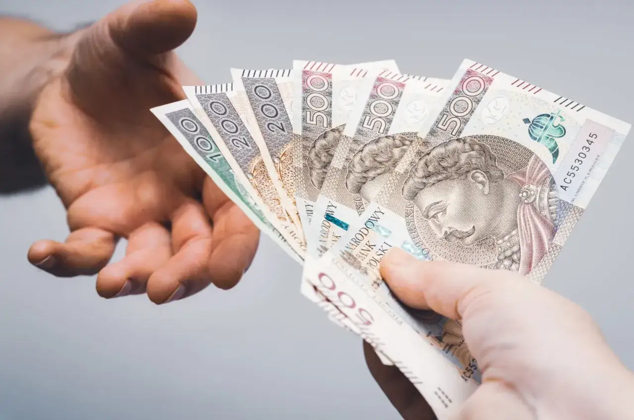 Dwie dłonie przekazują sobie polskie banknoty. Dowiedz się, jak wypłacić pieniądze z PPK.