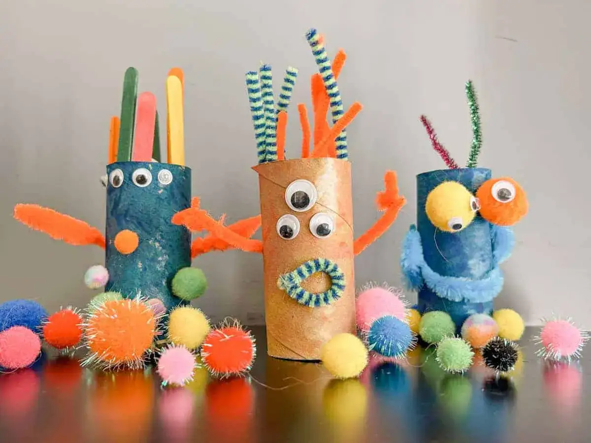Kreatives Basteln mit Klopapierrollen: Drei bunte Monster mit Pfeifenreinigern, Wackelaugen und Pompons.