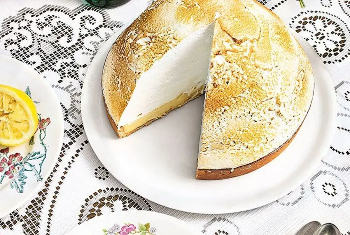 Tarte au citron meringu&eacute;e avec une cro&ucirc;te dor&eacute;e et une garniture blanche a&eacute;rienne. Une part est coup&eacute;e, r&eacute;v&eacute;lant la texture cr&eacute;meuse.